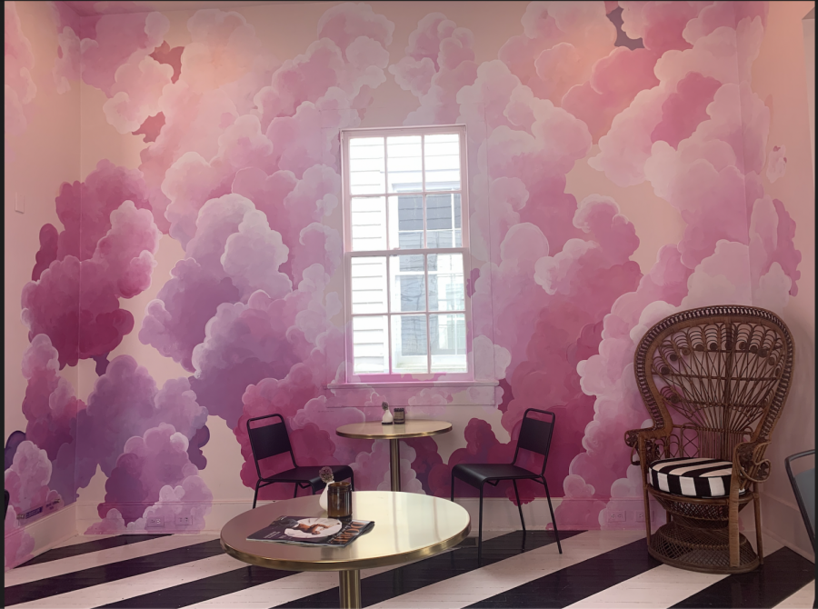 pink cloud art wall with a window in the center, black and white striped floor, table with two chairs, wicker chair in corner