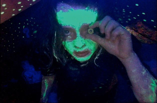 person with neon green on their face and arms holding a cheerio in front of their eye
