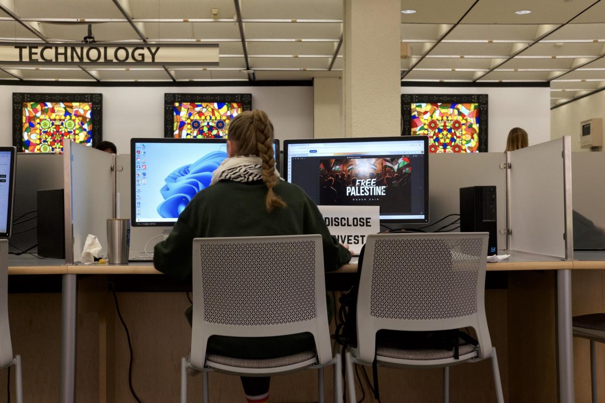 Tulane student wearing a keffiyeh studies at two computers, one of which reads, "FREE PALESTINE MAHER ZAIN." (Maher Zain is a Lebanese-Swedish singer/songwriter and producer.) Taped to the monitor is a sign that reads, "DISCLOSE DIVEST."