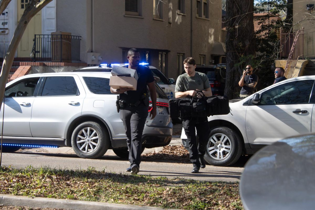 Law Enforcement Officers carry boxes and a bag out of a house after executing a search warrant